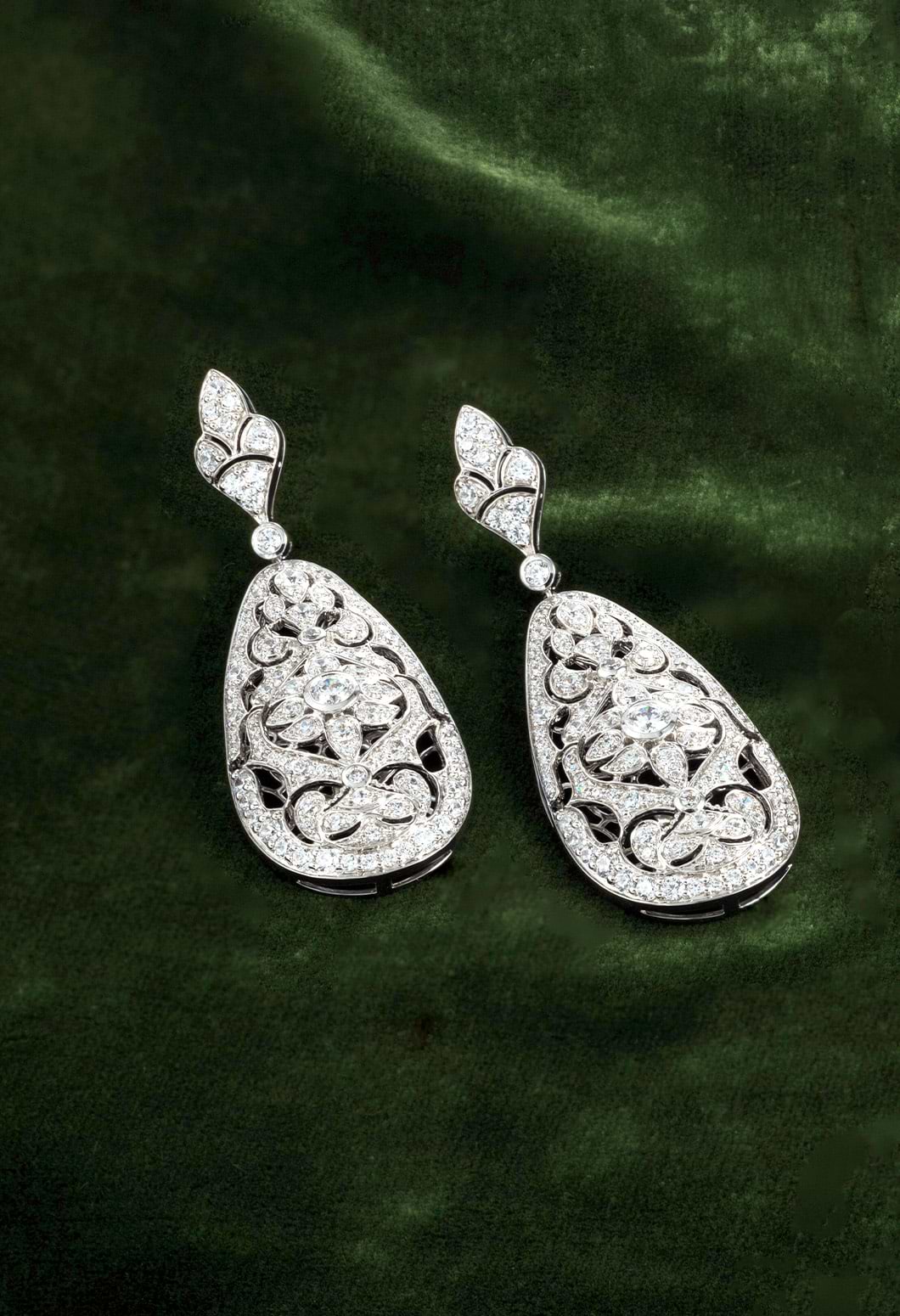 A pair of diamond drop earrings featured on a green background