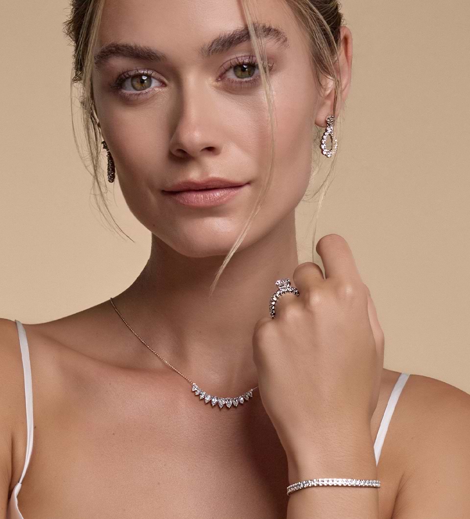Een close-upafbeelding van een model met modieuze diamanten oorbellen, een halsketting en een armband en ring aan haar linkerhand