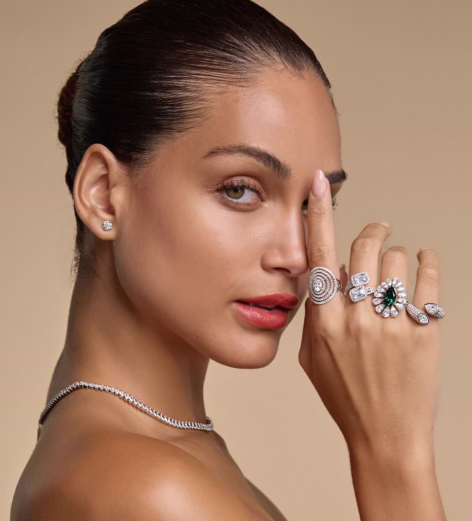Models face featuring diamond studs, necklace and four rings on her hand