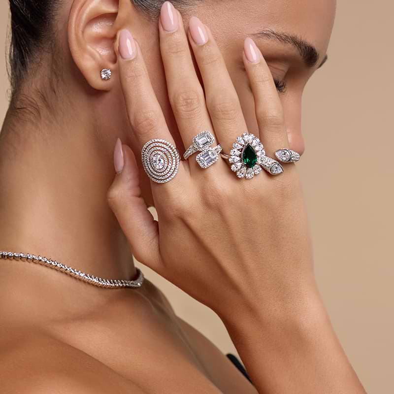 A woman wearing four different types of fashion rings on her hand while covering her face
