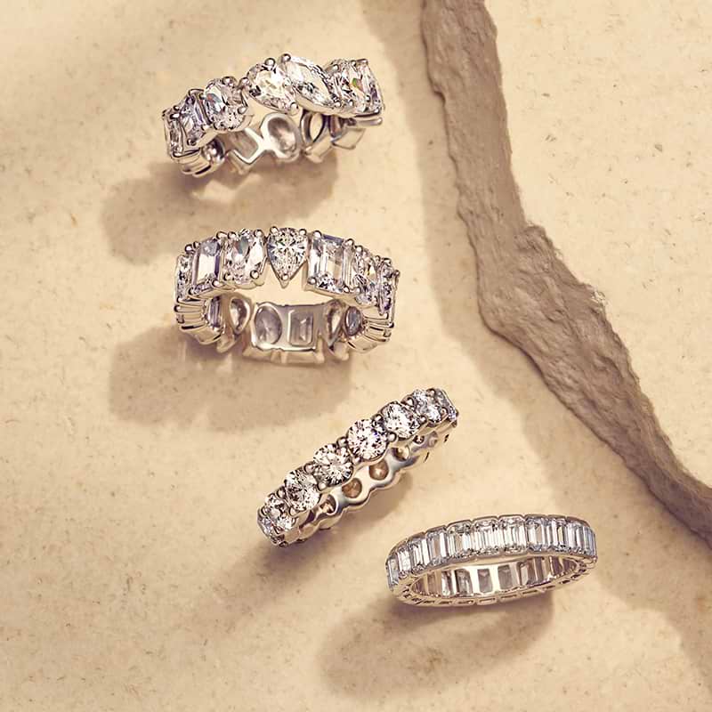 Vier verschiedene Arten von Eternity-Ringen auf einer beigen Marmoroberfläche