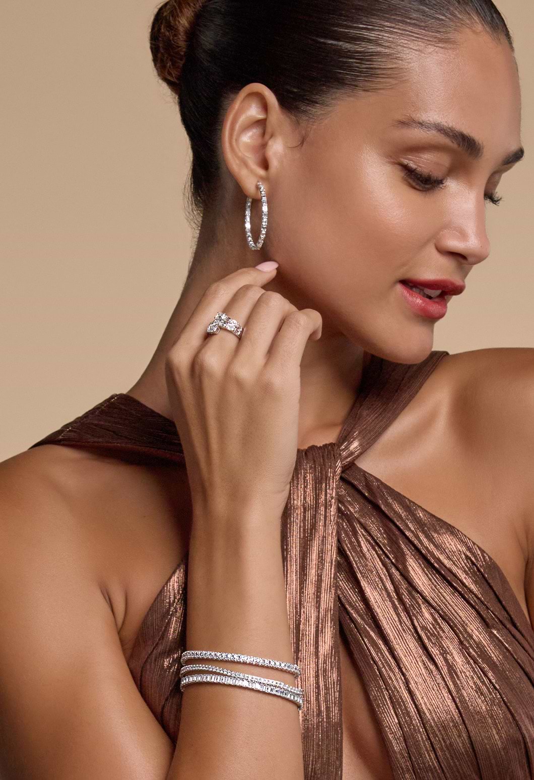 Image of a female model's side profile with three tennis bracelets on her right hand, one fashion ring and diamond hoops