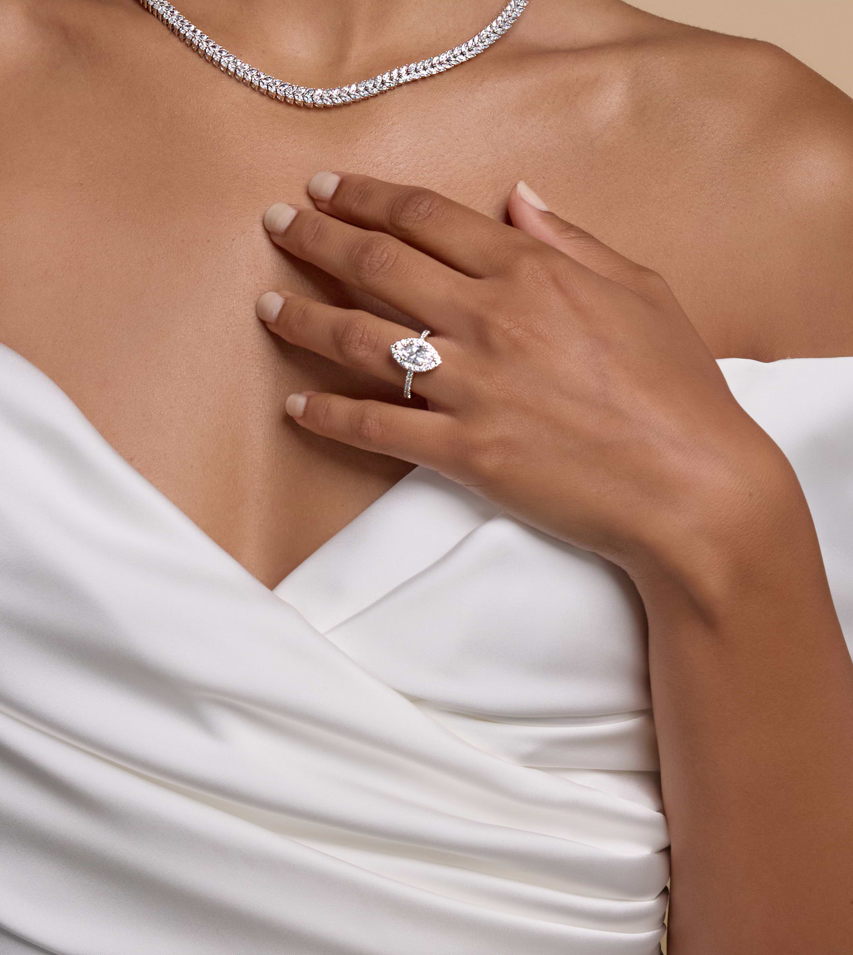 Image of woman's neck with diamond necklace and her hand gently placed against her chest featuring a diamond ring