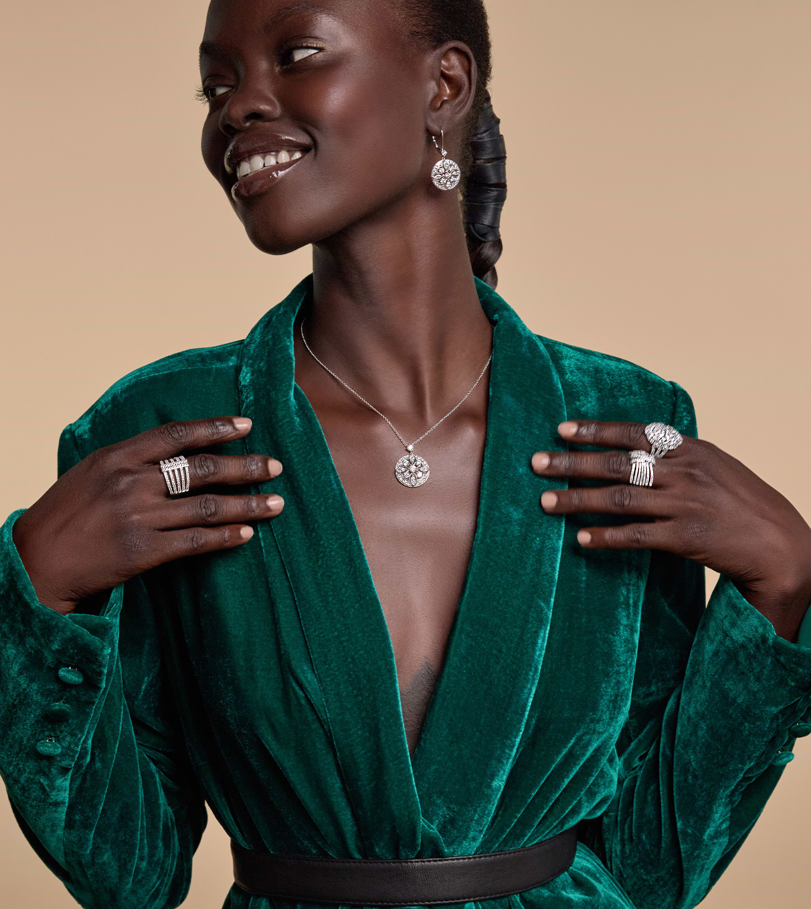 Bild einer lächelnden schwarzen Frau mit Händen auf beiden Seiten ihrer Brust und einem Diamantohrring, einer Halskette und Ringen