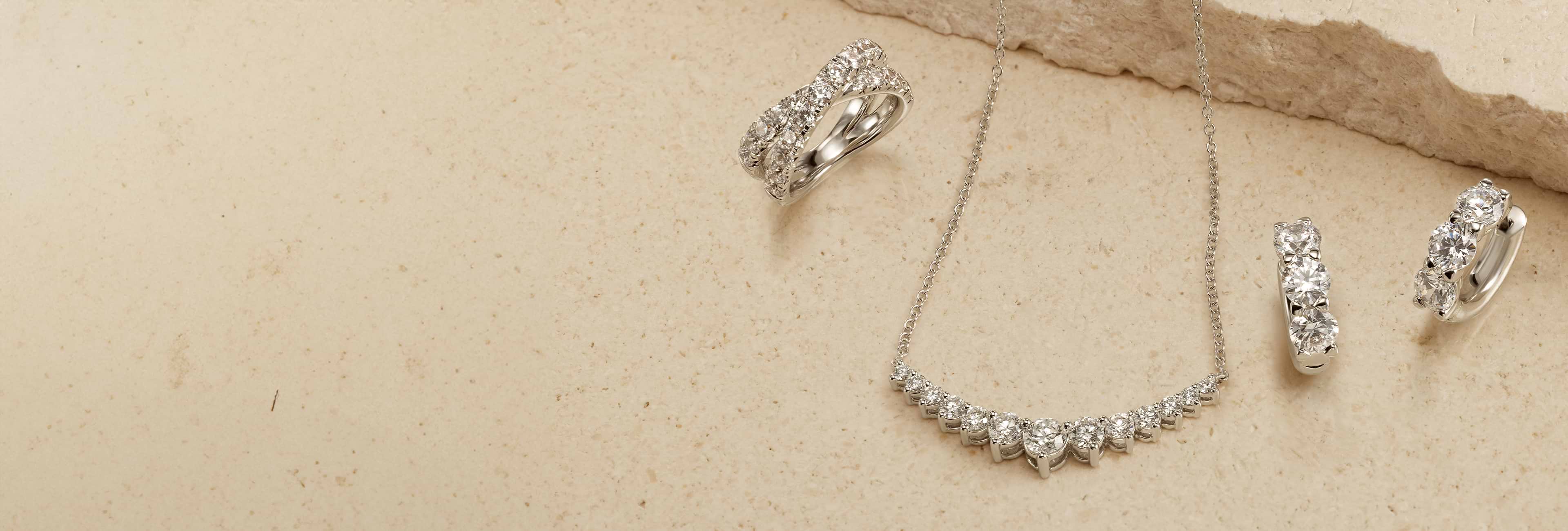An landscape image featuring a diamond necklace and three diamond rings with a neutral background