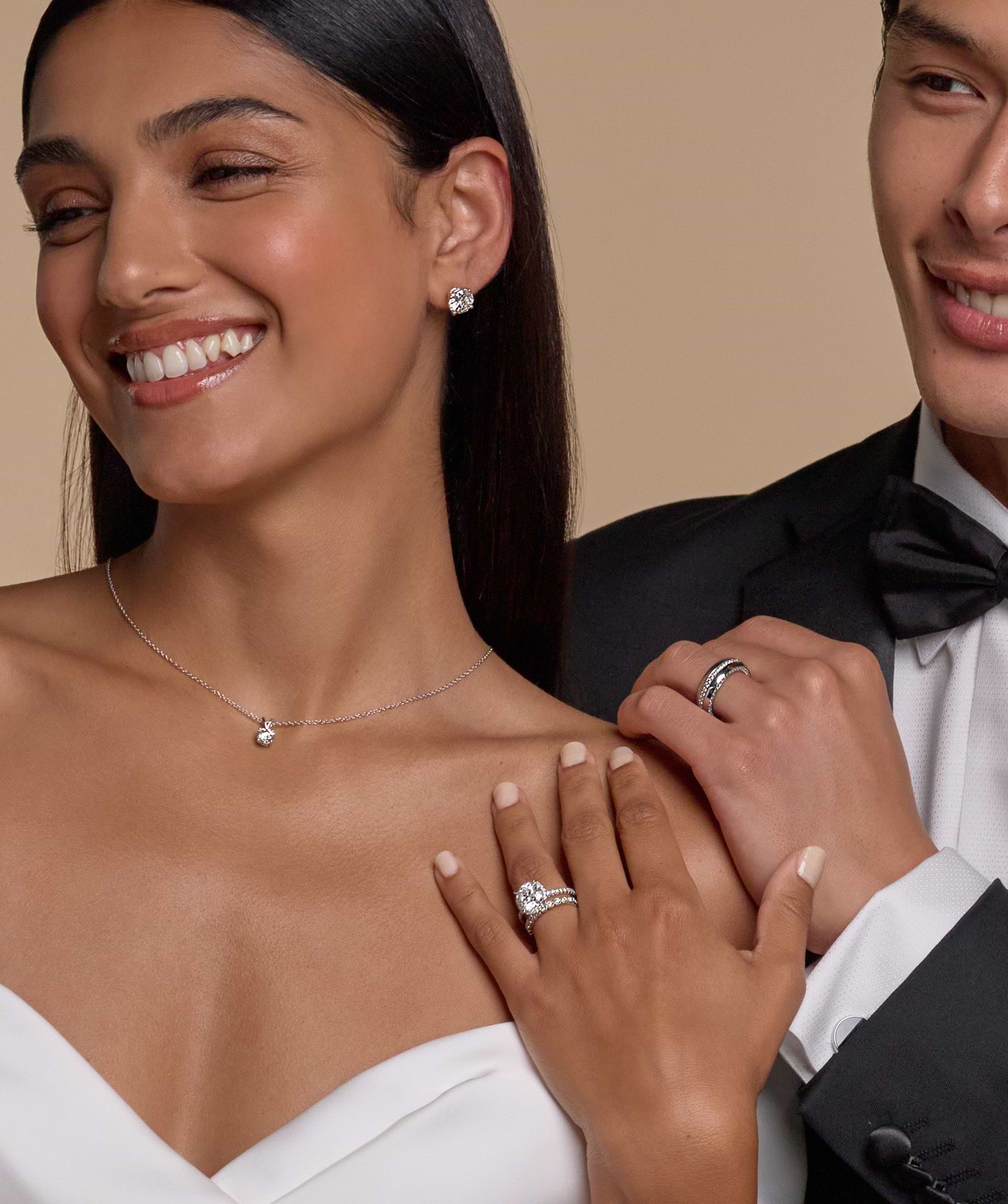 A smiling couple with the man wearing a wedding band and the woman wearing diamond earrings and necklace